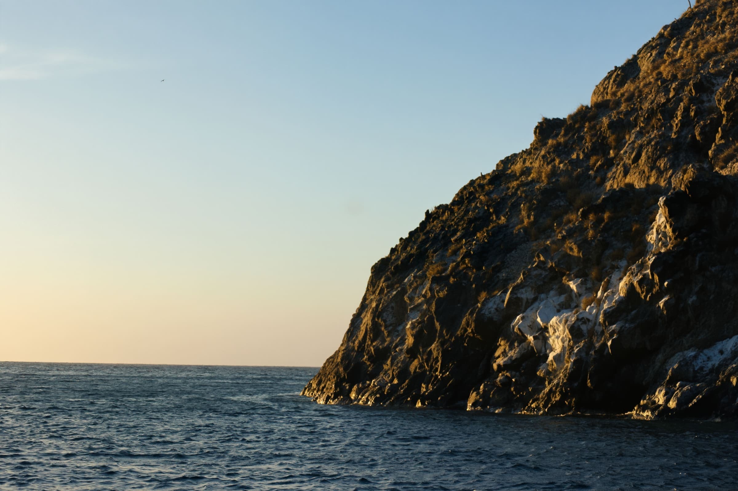 Farallón de roca junto al mar al atardecer, con el horizonte despejado